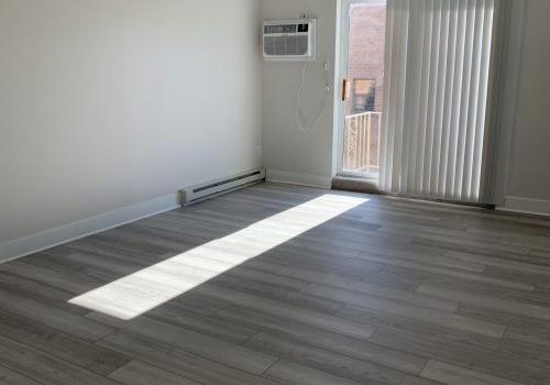 An air conditioning unit sits on a wooden floor in a room with white walls and wood floors